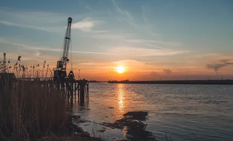 Sunset over a wide river with an old crane silhouetted on a pier among the reeds